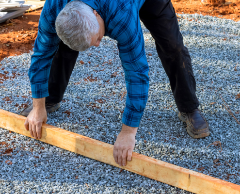 Shed foundation preparation by man with board and gravel