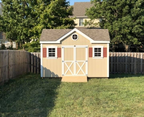 shed that's light tan with red shutters and white trim in a backyard